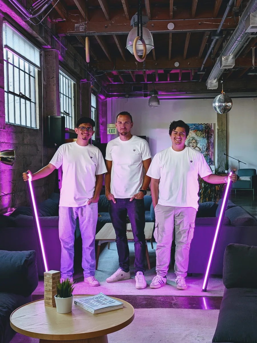 Founder and CEO Christian Byza standing in the center of the BePurple founding engineering team, three people in white BePurple t-shirts in a purple-lit loft office.